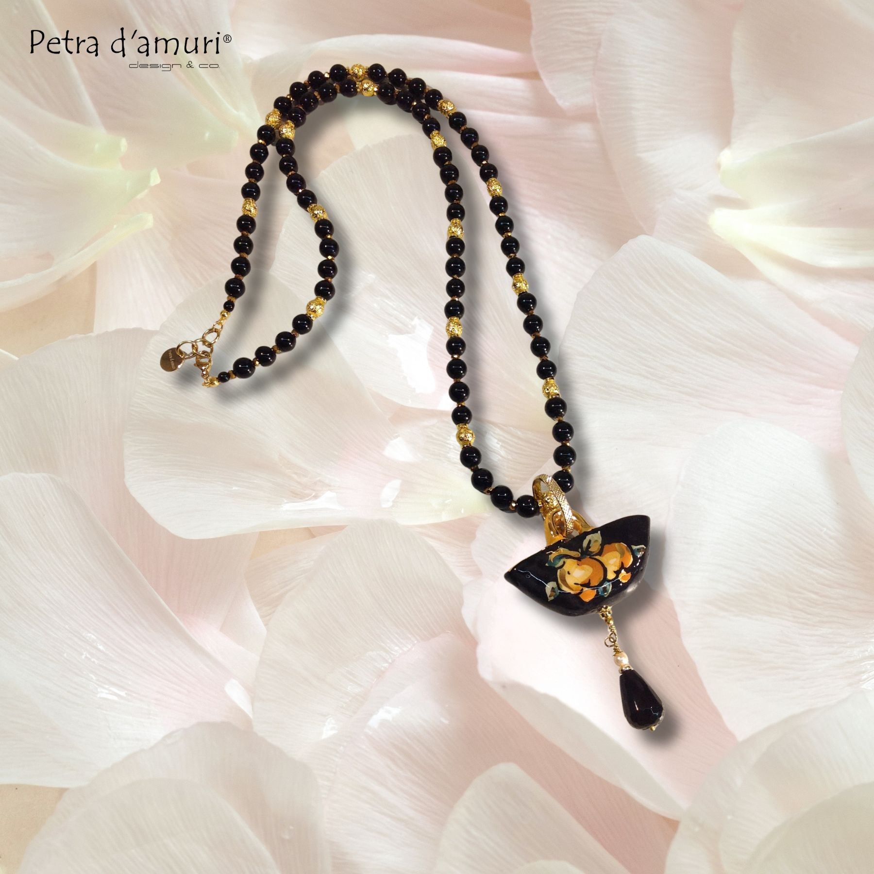 Raffinata ed elegante collana lunga siciliana con Perle di Onice Nero, pietra lavica dorata mescolata a ematite dorata, cristalli e dischi di ematite dorati, Coffa in ceramica di Caltagirone dipinta a mano con motivi di limoni, e con terzo lustro in oro.